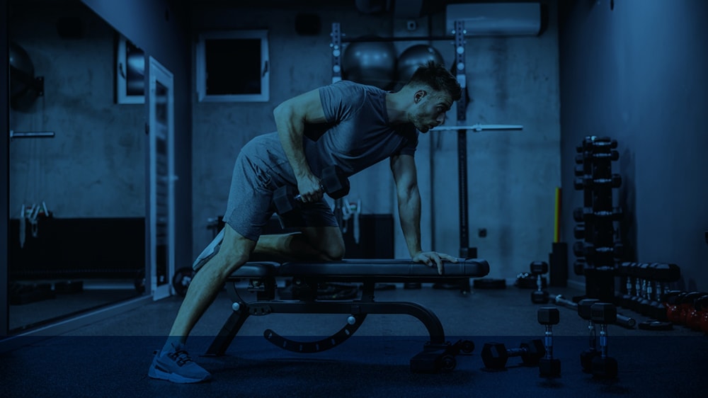 A man performing a dumbbell row in a small gym