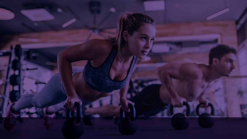 Close up of a man and woman both doing kettlebell push-ups at a gym