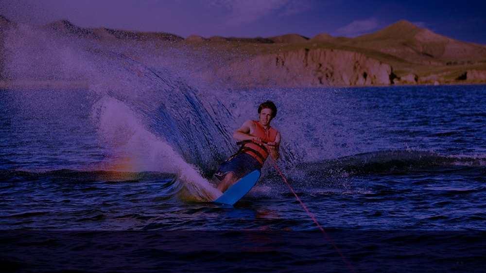 A man waterskiing with small mountains in the background